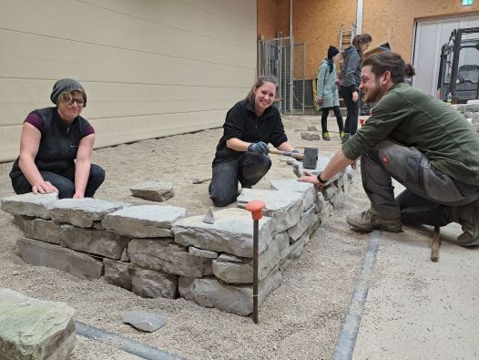 Abendschüler*innen erstellen in der Praxishalle für Gartengestaltung ihre erste Mauer aus Natursteinen